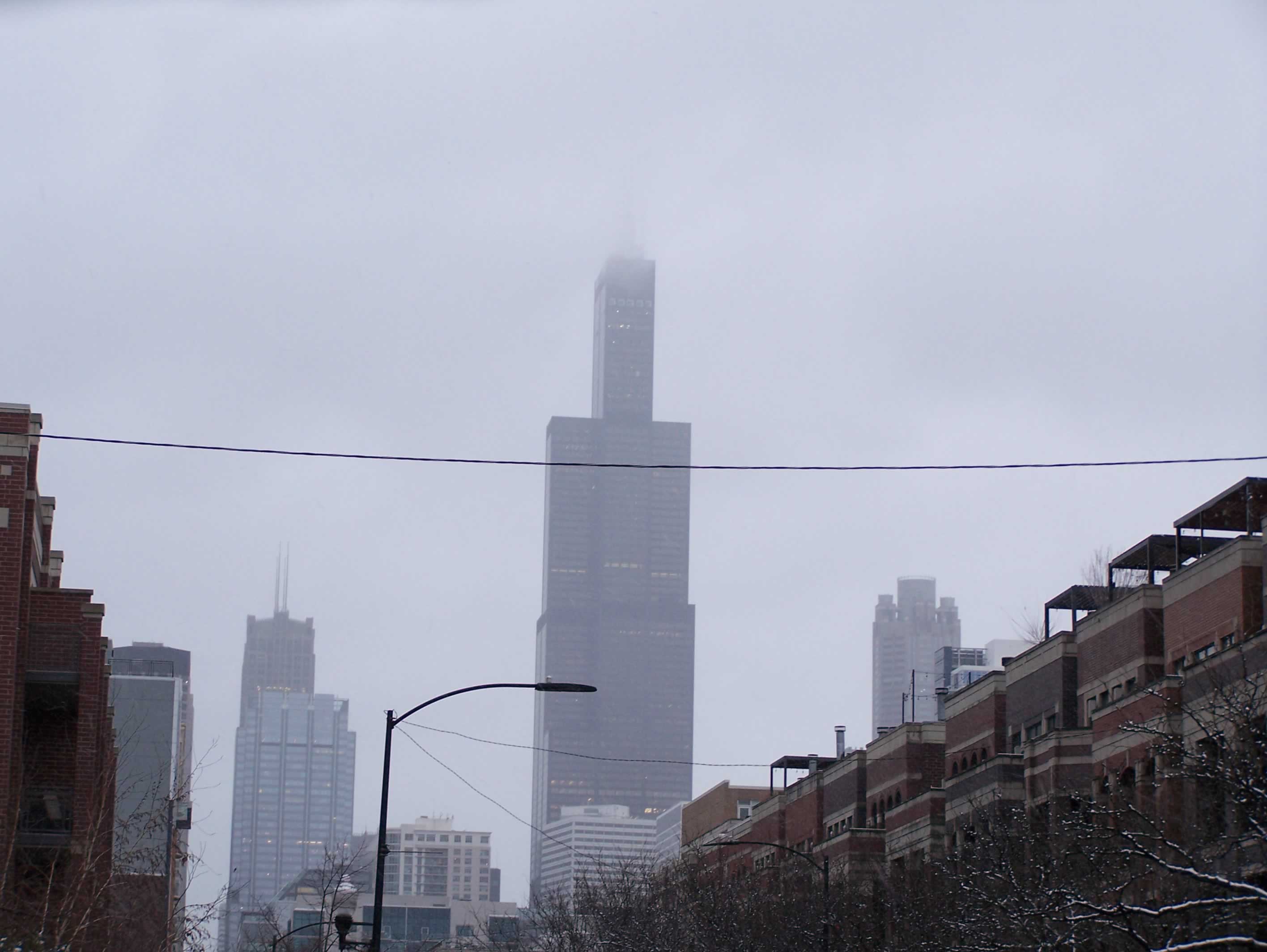 The Sears Tower rises out of the Chicago skyline, peaking into the dense foggy overcast sky.