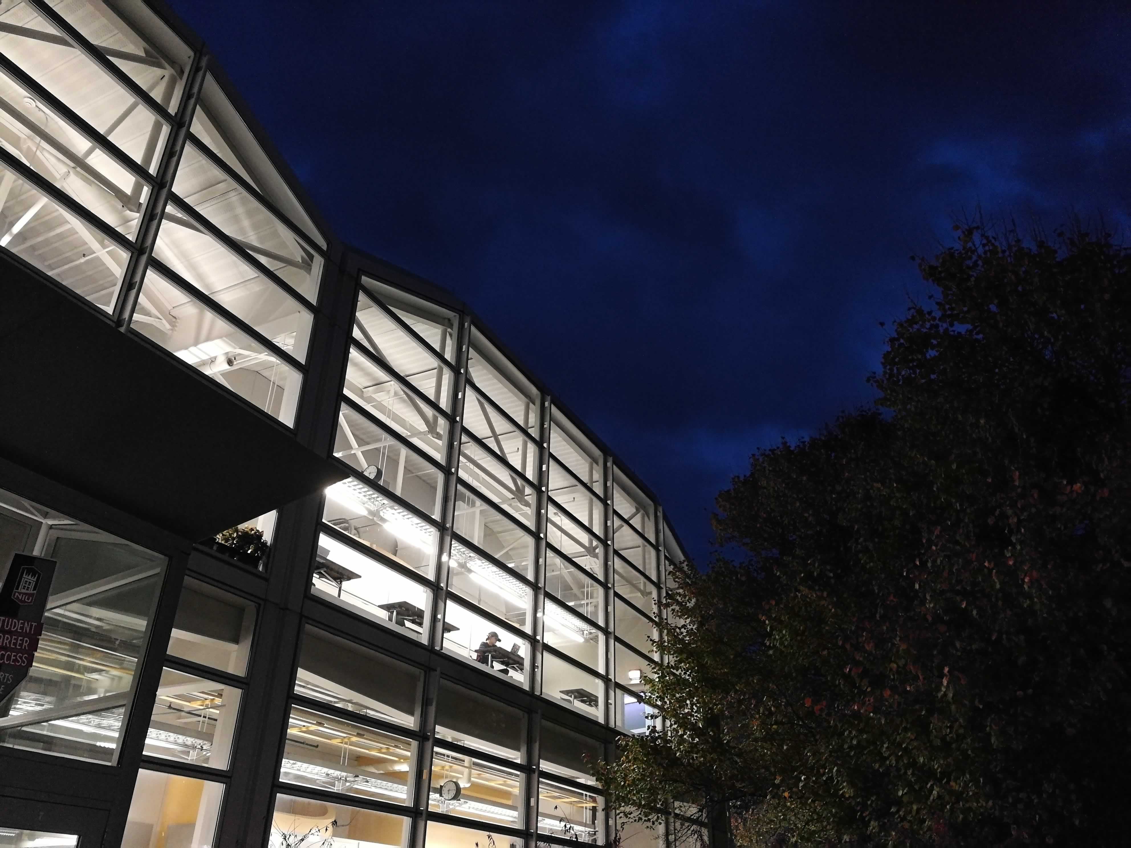 A geometric facade made of windows is brightly lit up against an oddly blue night sky.