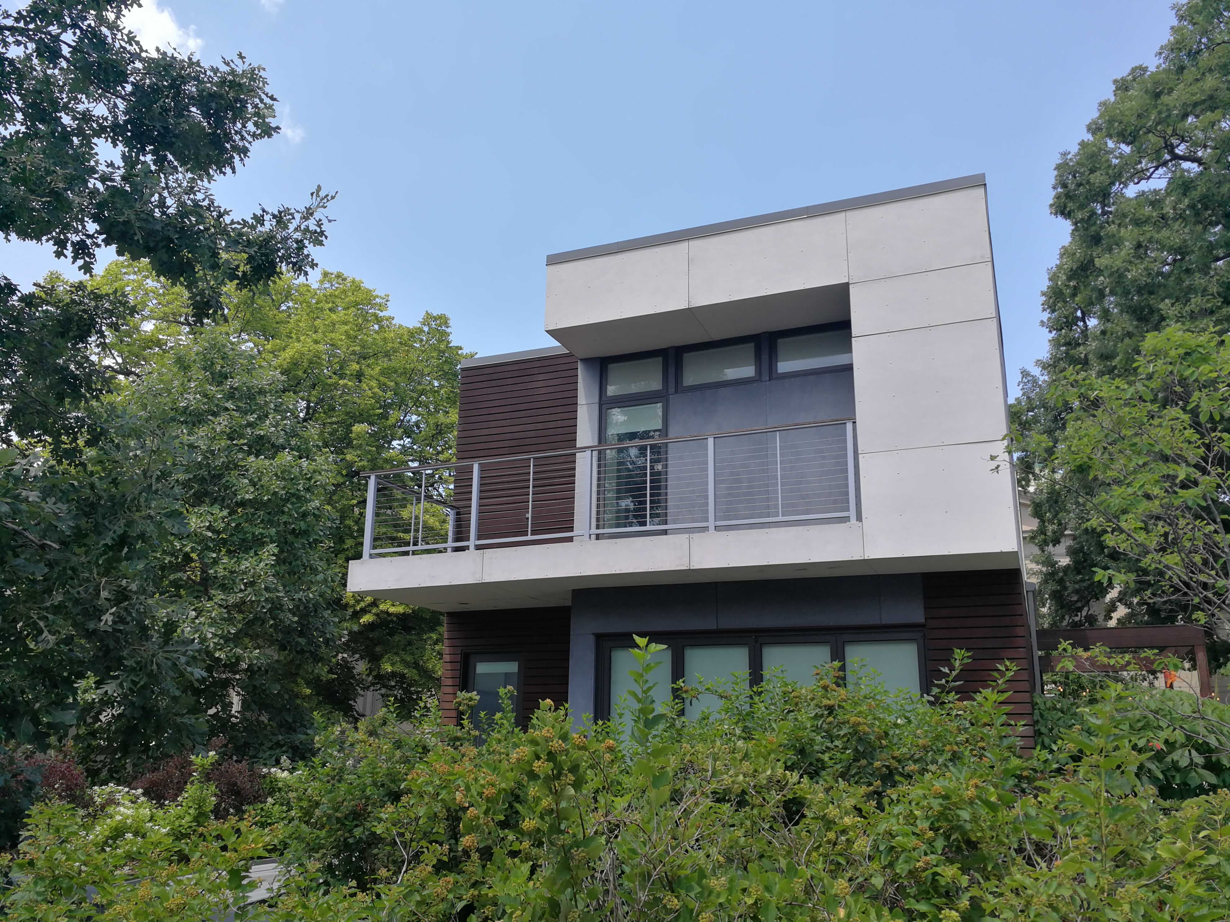 A stylish modern house made from concrete, metal, and wood, sitting in a lot of greenery.