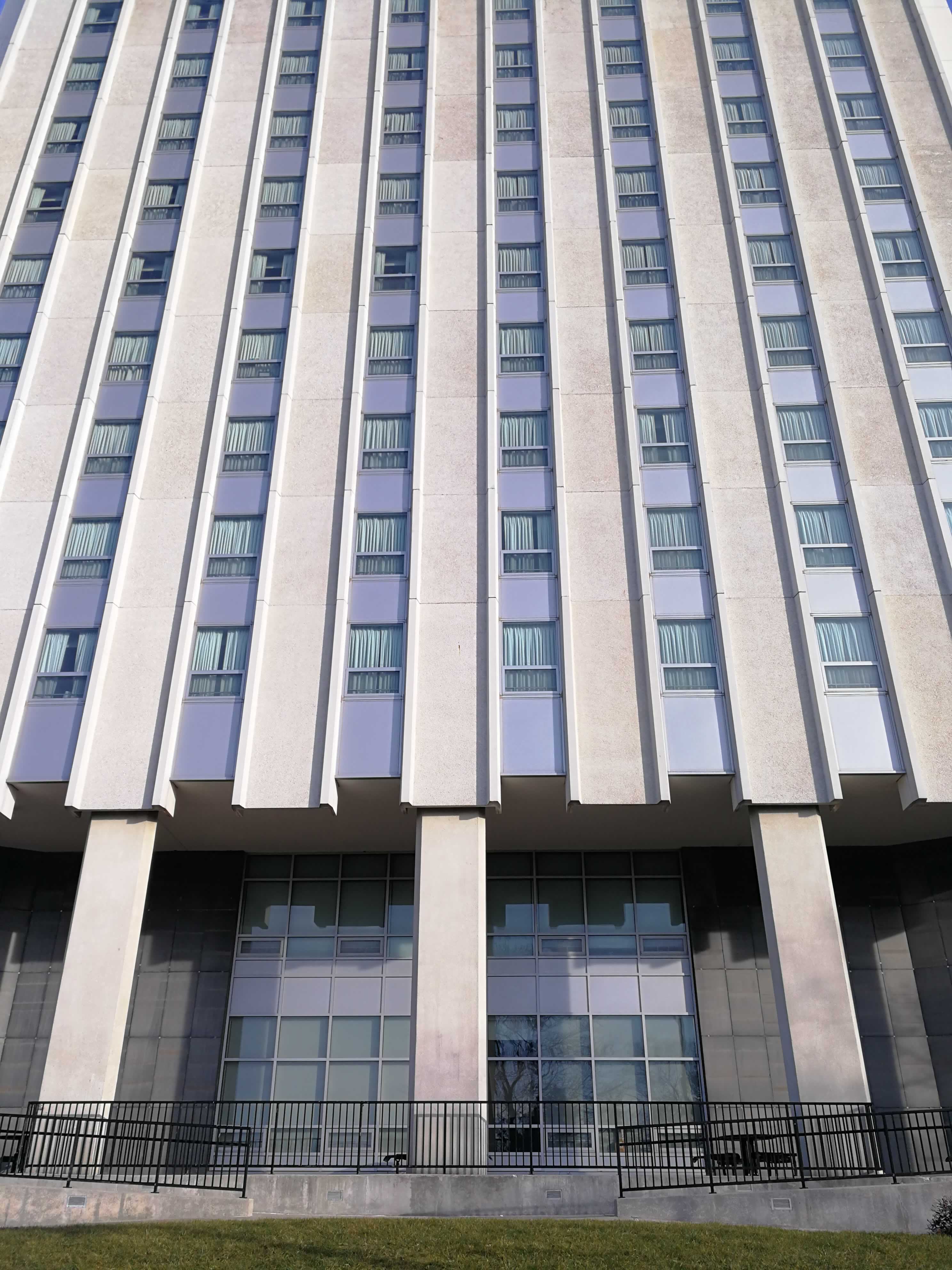 Striking columns of concrete rise beyond the top of the photo, with metal plates and windows running the span between them.  The columns abruptly stop about 20 feet off the ground, as they are cantelevered by the smaller inner core of the building.